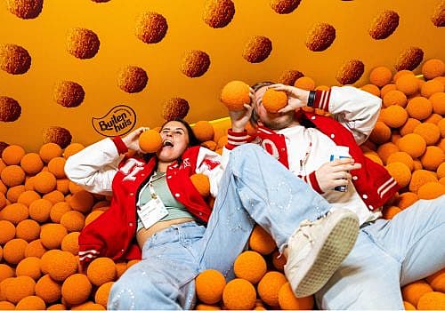 Twee mensen liggen tussen oranje bitterballen in een interactieve stand