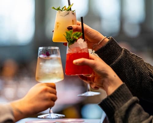 Drie mensen proosten met kleurrijke cocktails in een gezellige, moderne setting