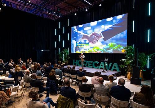 Presentatie in het Horecava Theater met spreker op het podium en publiek in de zaal
