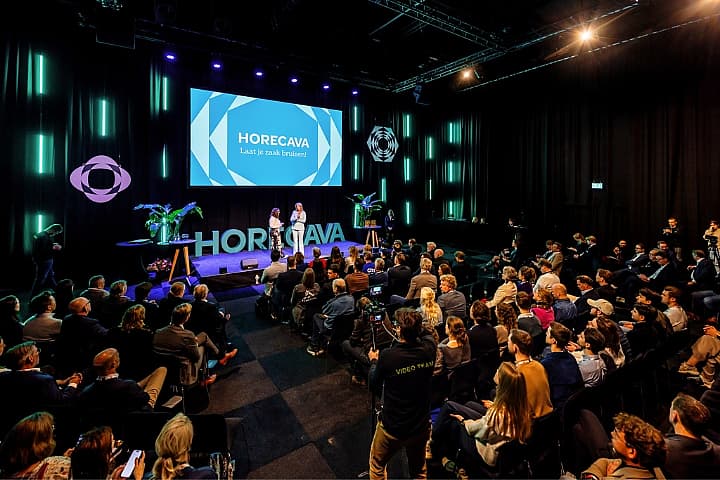 Bezoekers zitten in een vol theater tijdens de opening van Horecava 2025, terwijl Pernille La Lau en Inga Blokker op het podium staan