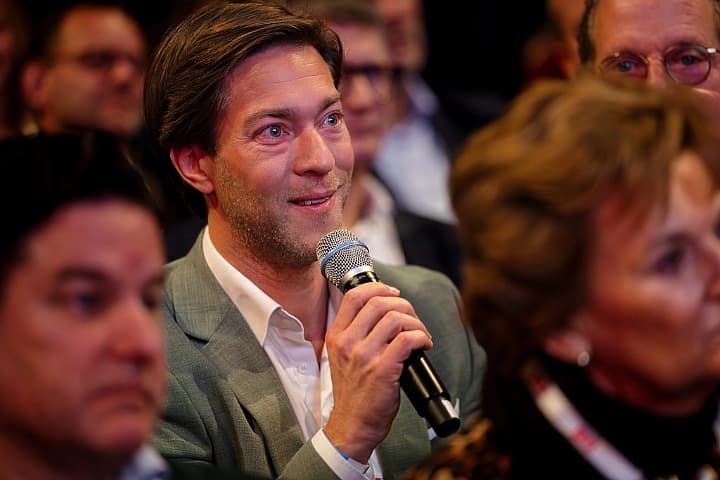 Theaterbezoeker stelt een vraag met een microfoon in de hand, omringd door andere toehoorders