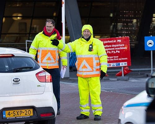 Twee verkeersregelaars in veiligheidskleding begeleiden het verkeer bij een parkeerterrein