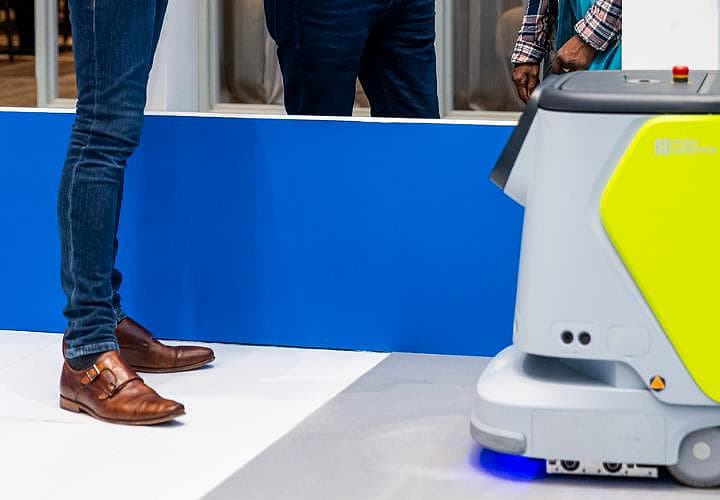 Beursbezoekers staan naast een autonome schoonmaakrobot die over de vloer rijdt.