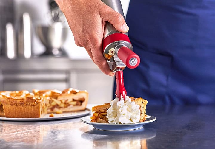 Hand spuit slagroom op een stuk taart in een professionele keuken